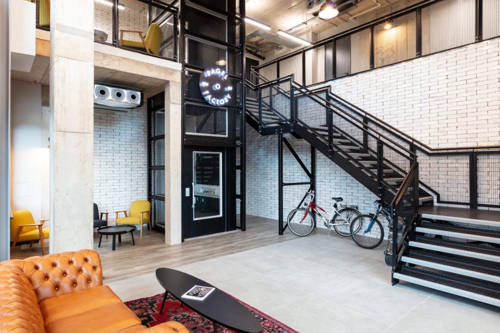 Workspace stairwell with branded lighting graphic, wheelchair access lift, seating area, sofa, coffee table and bikes stored under the stairs.